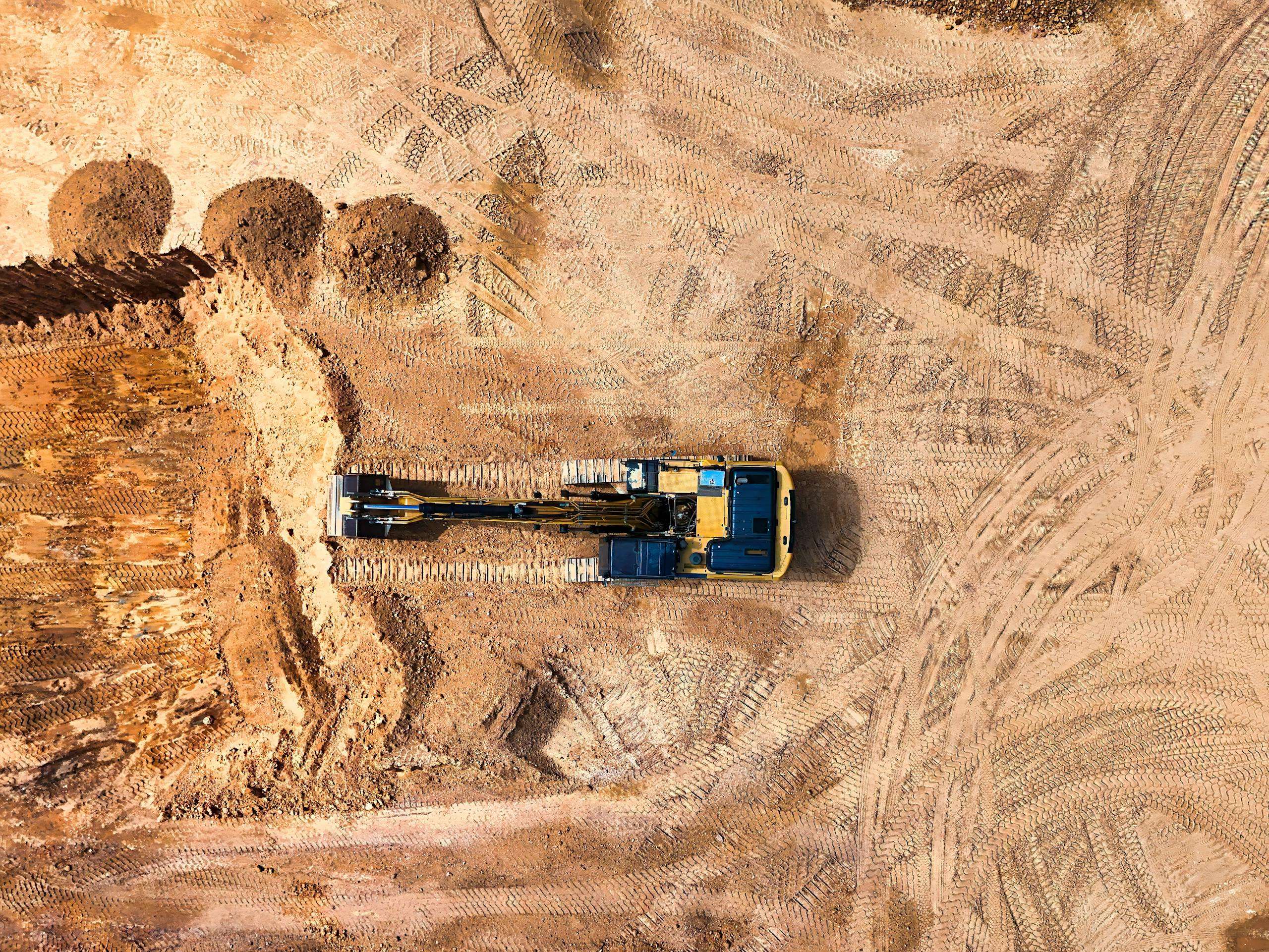 Aerial photo of an excavator working on a large empty construction site.
