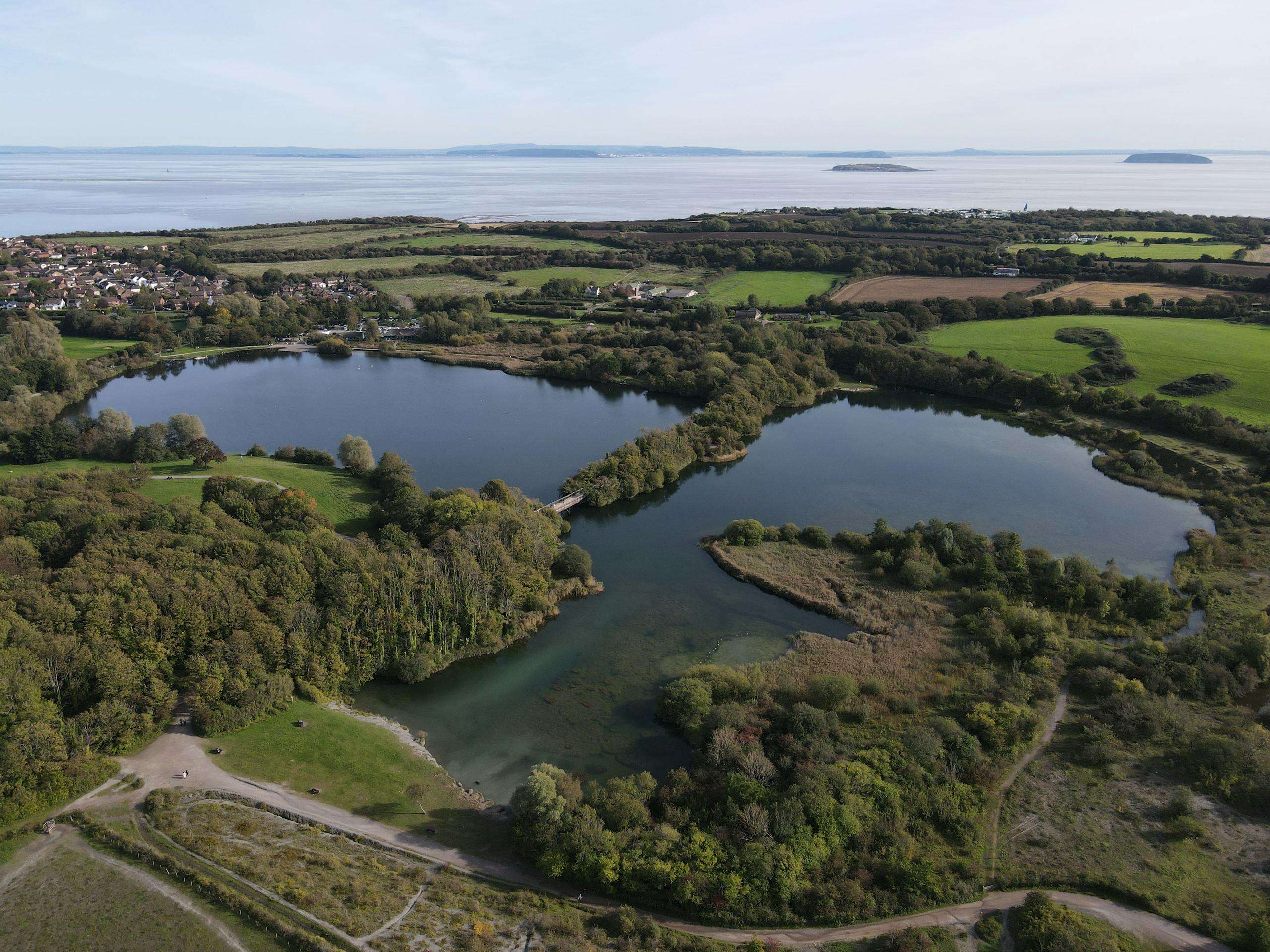 Aerial shot of Cosmeston Lakes with green landscapes, dense trees, and serene water bodies in Wales.