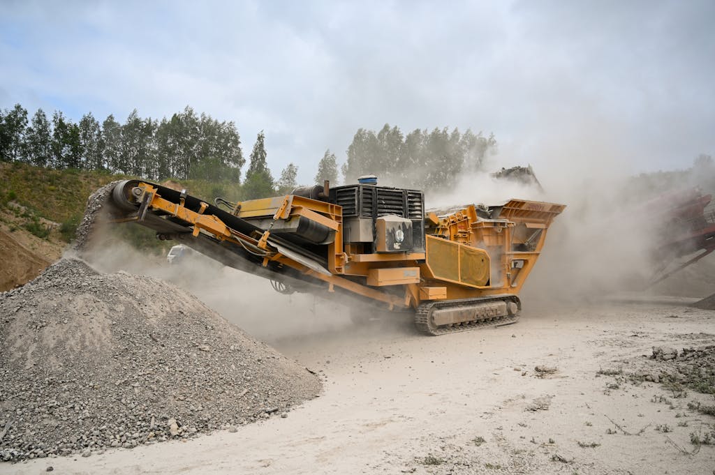 Heavy-duty crusher machine processes materials in dusty quarry amidst greenery.
