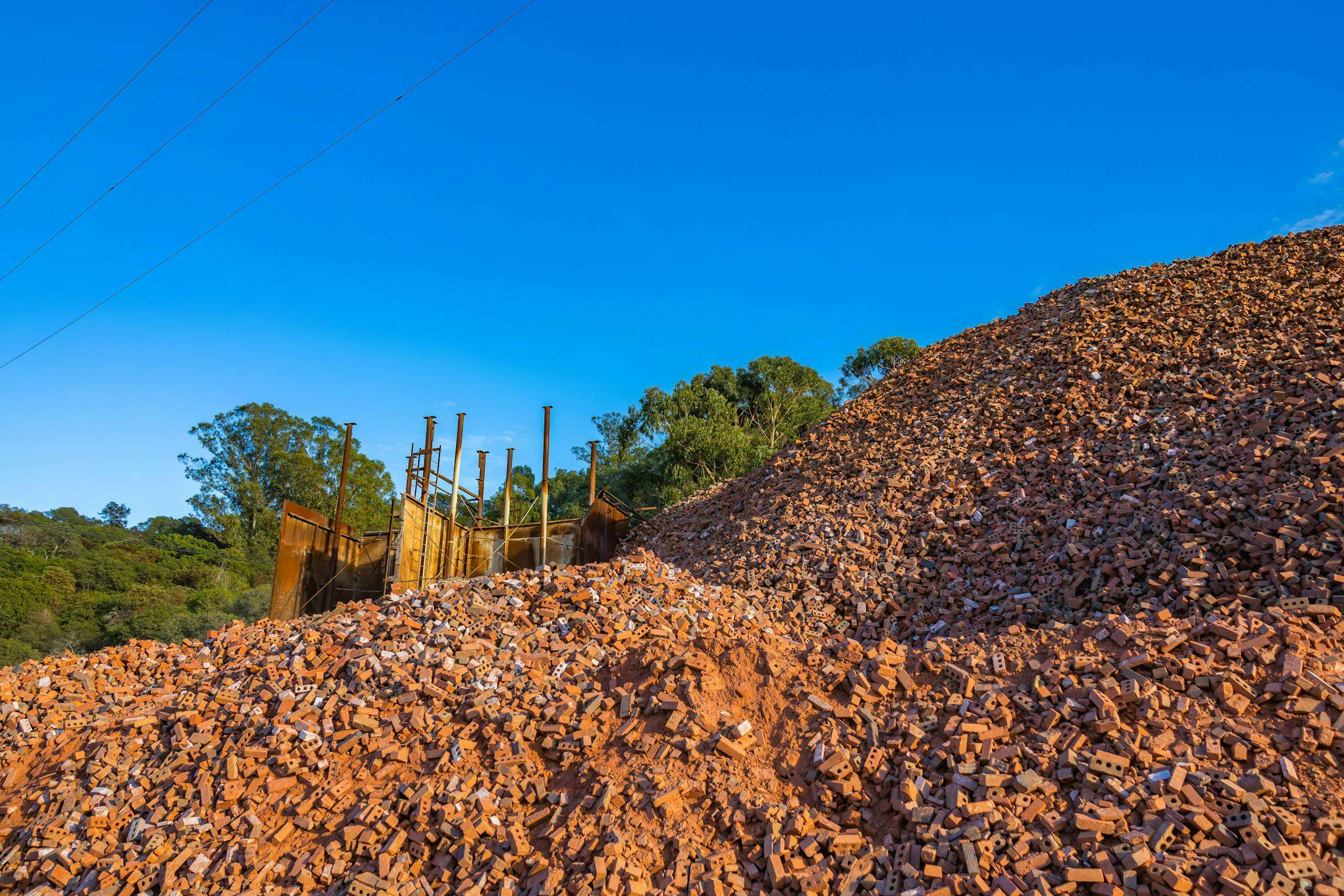Large pile of red bricks at a construction site under clear blue sky.